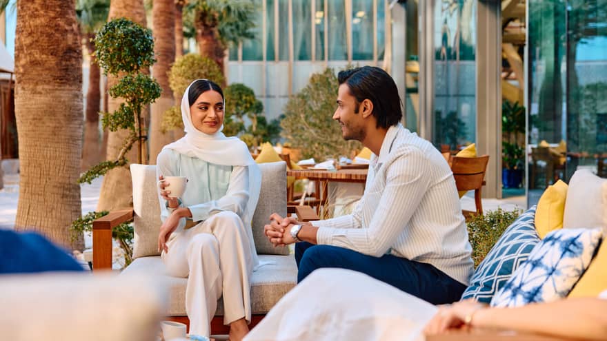 A couple sits in an outdoor lounge seating are smiling at each other