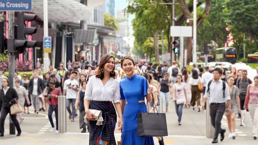 two well-dressed women carrying shopping bags and walking through a busy street in singapore