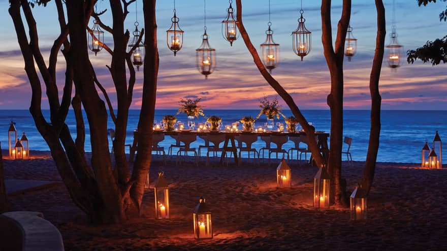 Lanterns hang from trees near dining table on Manzanillas Beach at sunset