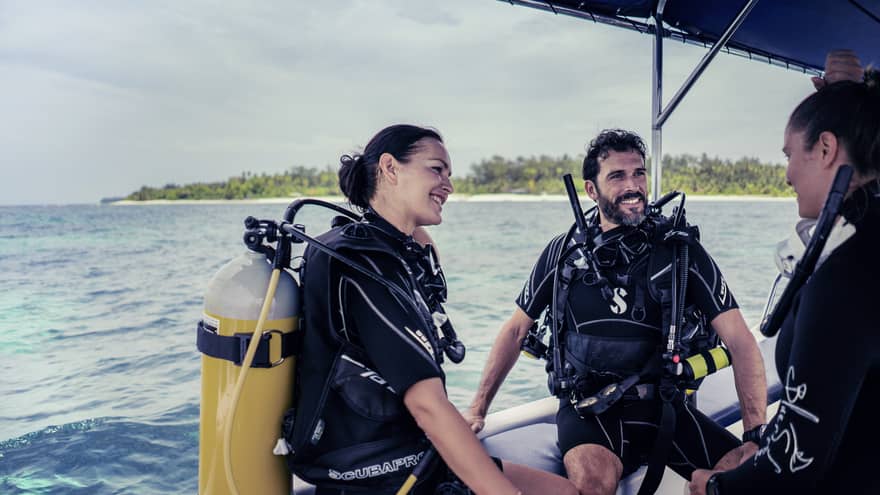 Three people in SCUBA gear with tanks on boat in ocean smiling and talking 