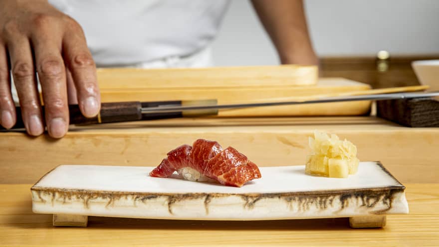 Edomae sushi on a modern stone plate, with a chef and chef's knife in the background