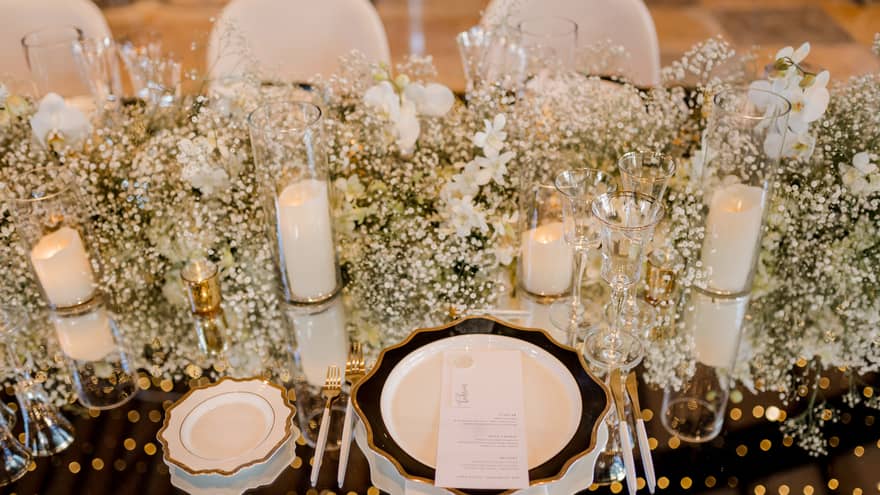 Closeup of table set for wedding reception with white flowers, candles, chair covers and dishes