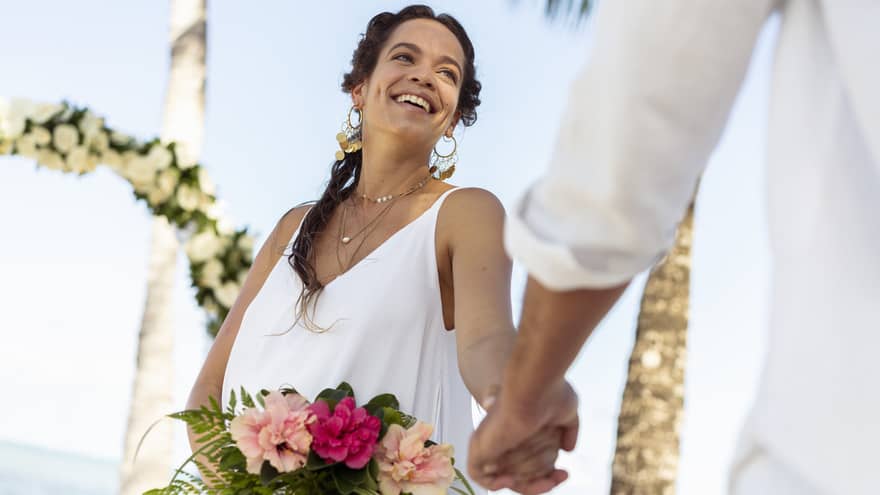 Smiling bride holds tropical flower bouquet, holds hands with groom out of frame