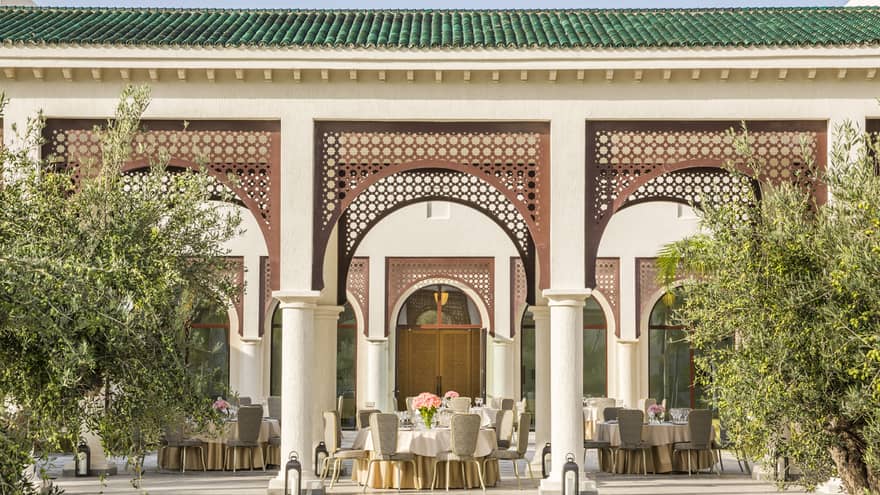 Round tables and chairs with vases of flowers set on covered patio with trees, lanterns 