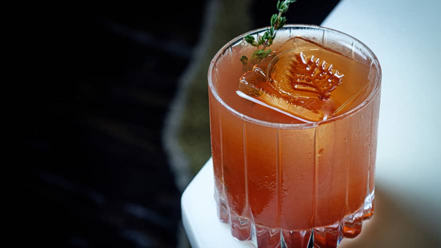An amber coloured cocktail with a leaf imprinted into the ice.