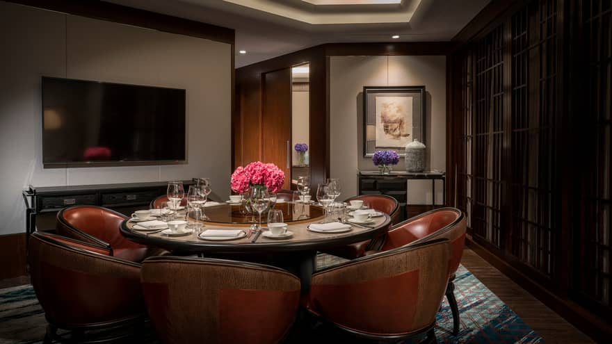 Dark red leather bucket seats around round dining table in business meeting room, TV on wall