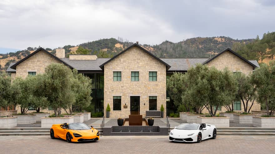 A white sports car and an orange sports car are parked in front a stately stone building