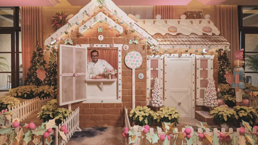 Chef stands inside of a life-size gingerbread house