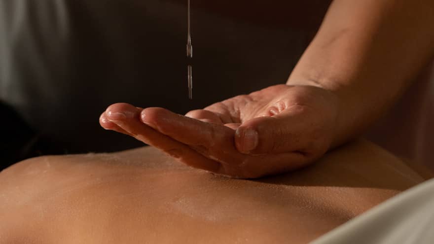 A spa practitioner pours oil into their hands in a massage treatment setting.