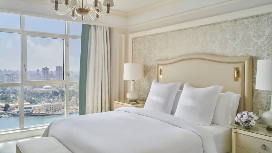 Guest bedroom with king bed, white linens and cream tufted headboard; floor-to-ceiling window with views of the River Nile