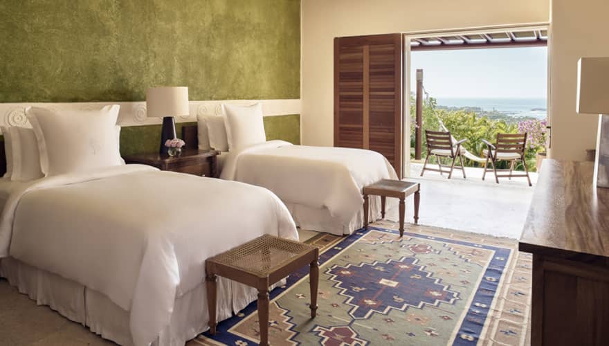Bedroom with two twin beds, green accent wall, small benches, walk-out terrace