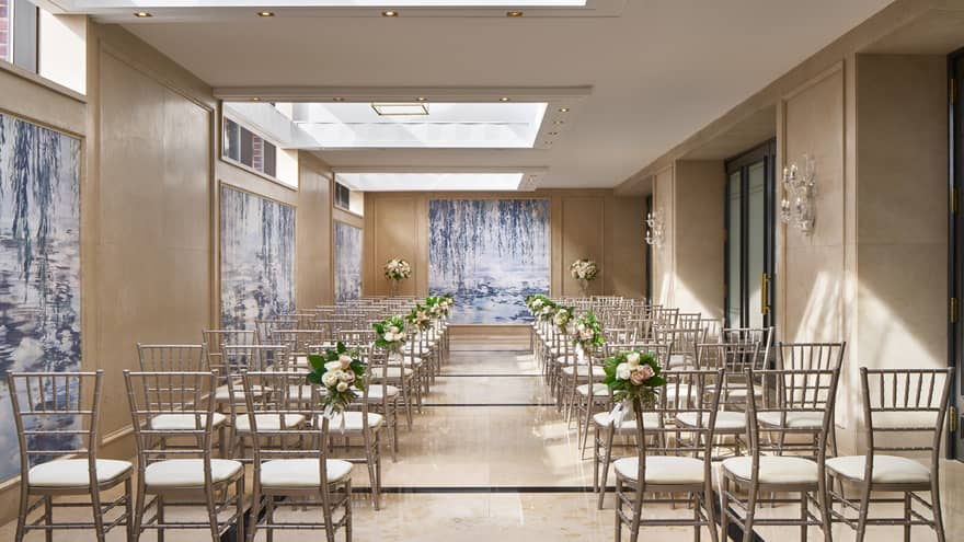 Rows of chairs under the ample skylights of Dumbarton Conservatory, decorated with wedding flowers.