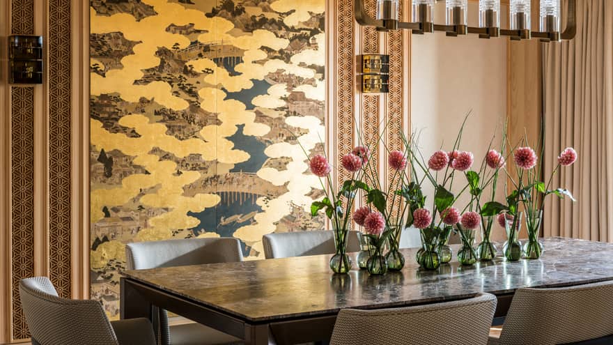 Elegant dining area with a large table decorated with pink flowers in small vases and a gold-accented wall panel