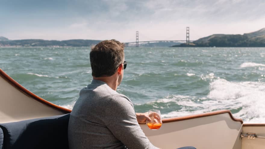 A man enjoys a drink as he relaxes on a boat, the Golden Gate Bridge in the distance