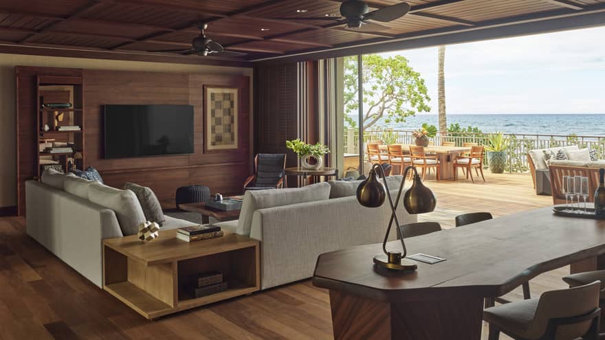 Wooden desk and living room with light grey sofa, full wall of windows with ocean view