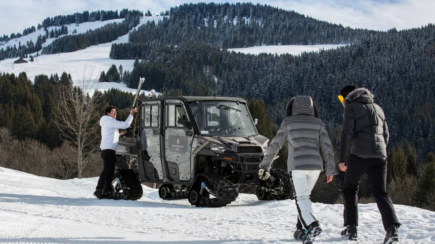 Two people in snowsuits walk toward ski concierge at large snowmobile