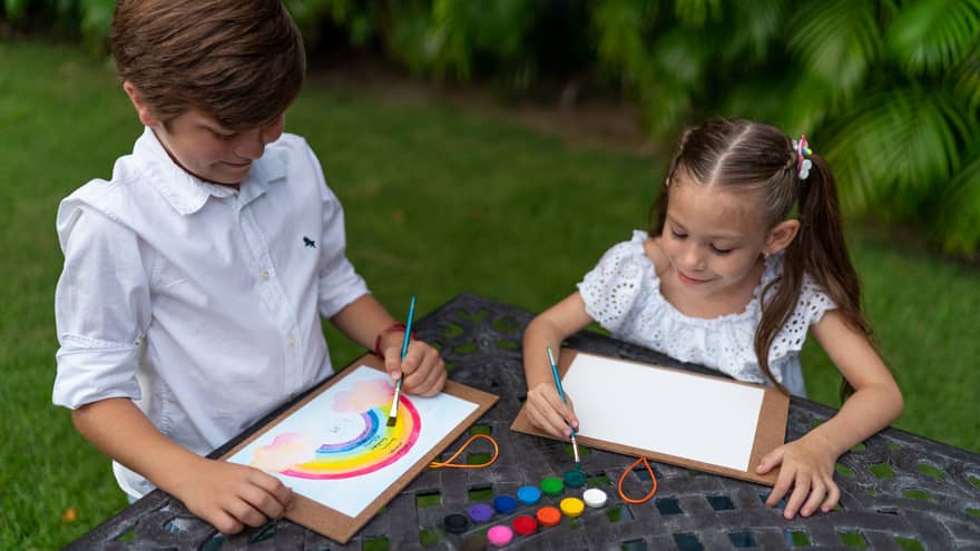 Two children painting with watercolour outside.