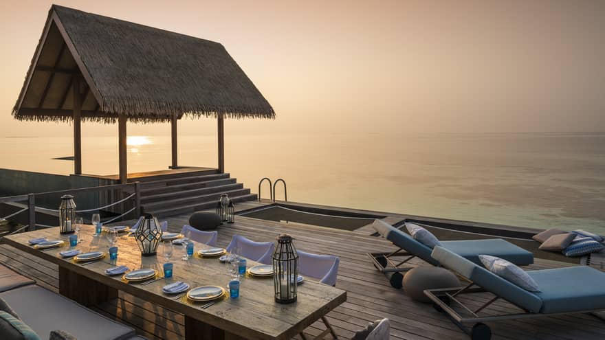 Two-Bedroom Water Villa thatched roof pavilion over long private dining table on deck at sunset