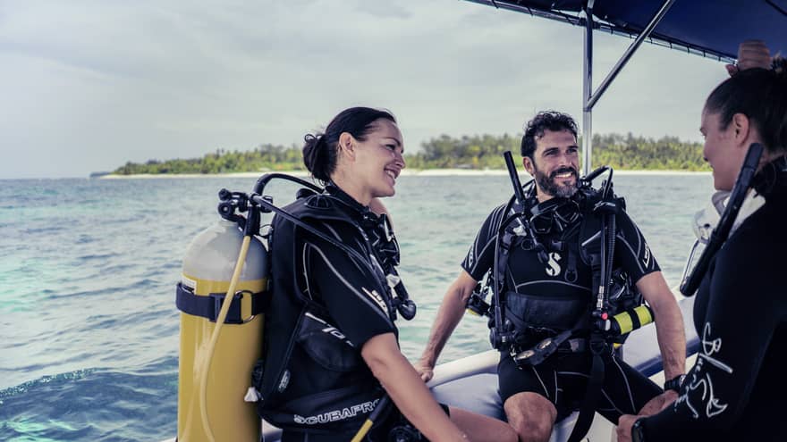 Three people in SCUBA gear with tanks on boat in ocean smiling and talking 