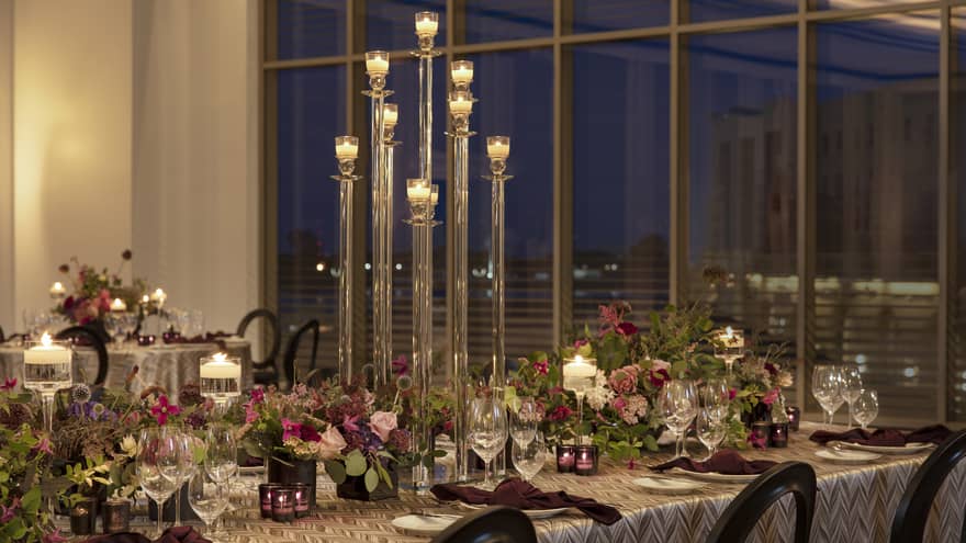 Long table in ballroom decorated with fuchsia centrepieces and greenery, tall candelabras, floor-to-ceiling window overlooking downtown New Orleans