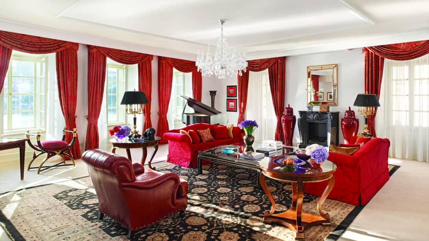 Presidential Suite with red sofas and armchair, red curtains on sunny corner windows, crystal chandelier 