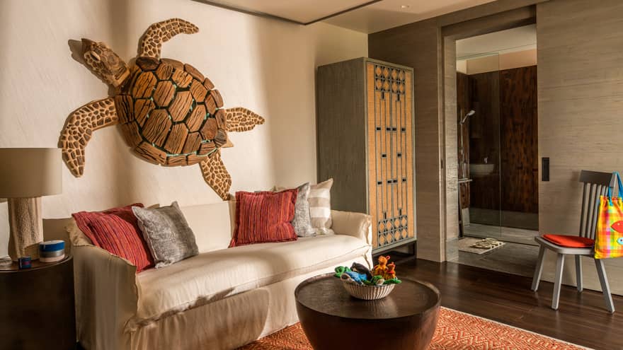 Large wood sea turtle sculpture hangs above sofa with red, grey cushions by cabinet