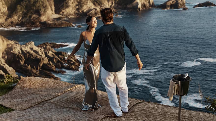 A couple standing near a vast, shimmering ocean against a backdrop of majestic cliffs, embraced by the beauty of nature