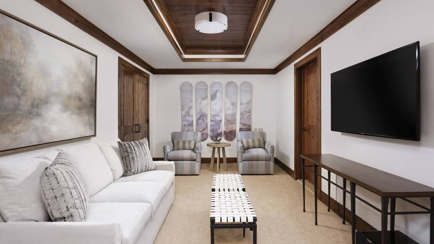 Guest room living area with cream sofa and twin striped armchairs, rectangular coffee table, wall-mounted flat screen TV, wooden accents