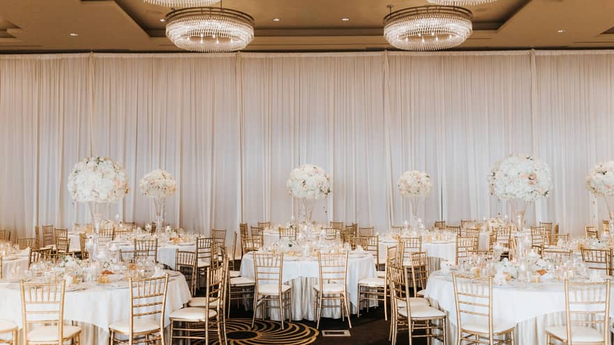 Elegant gold and white banquet dining tables in event room with small round chandeliers