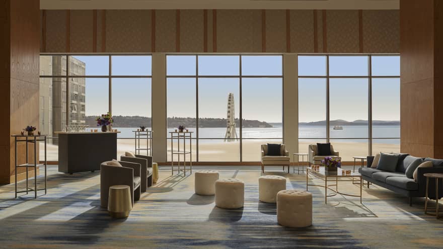A large room with sofas, chairs, standing tables, stools and large windows.