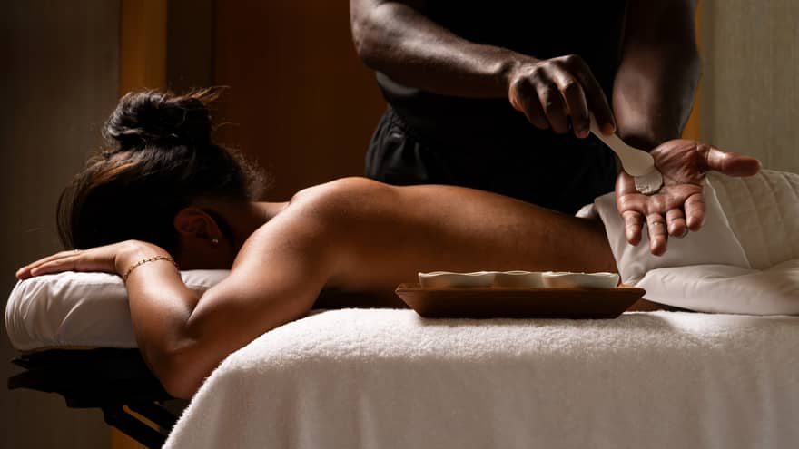 Guest laying on a massage table while the massage therapist prepares ingredients for massage.