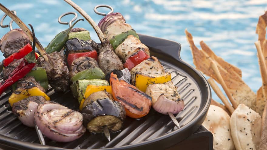 Kabobs on a grill with the pool in the background.
