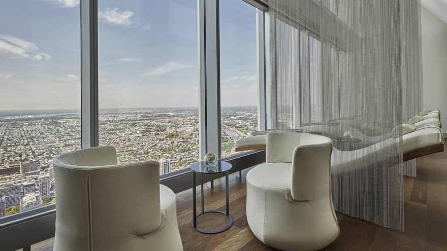 Lounge with two beige chairs and windows overlooking the city.