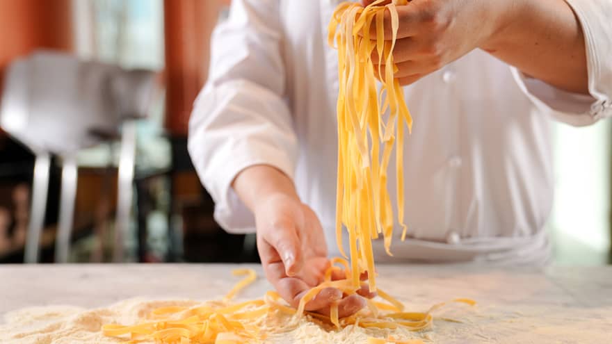 Close up of chef's hands holding a handful of pasta with flour and more pasta on the table below