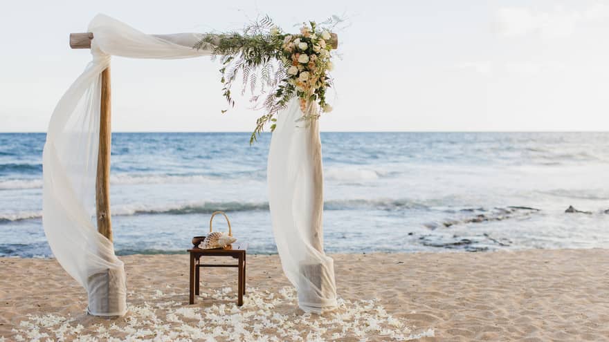 Sand beach wedding altar with flowers, white linens flowing in breeze
