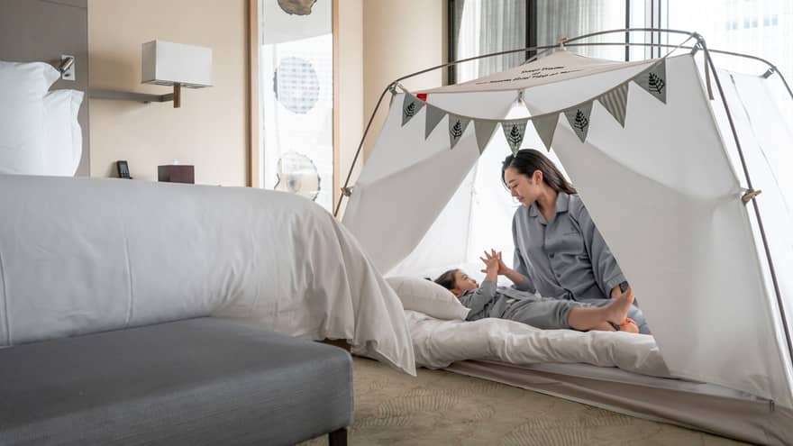Parent and child in pyjamas playing together inside a cozy tent with bunting decorations