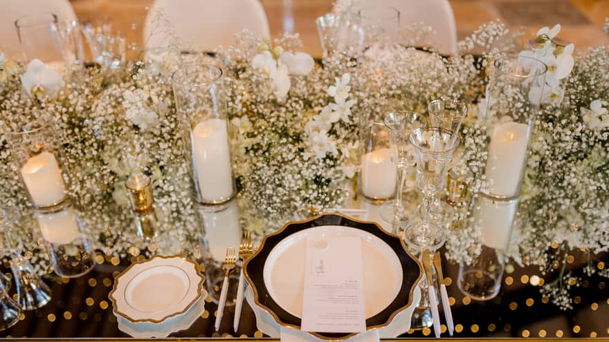 Closeup of table set for wedding reception with white flowers, candles, chair covers and dishes