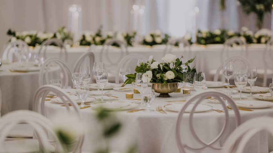 Round tables set for wedding reception with white linens and small floral centrepieces