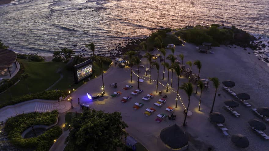 A bird's eye view of cars watching. a screen on a beach.