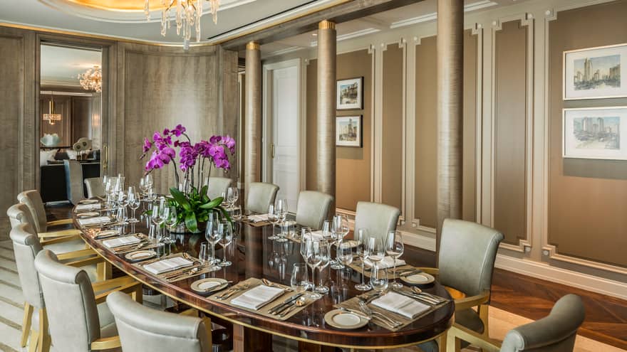 Long oval private dining table with 12 grey chairs, purple orchids in centre, elegant grey pillars, wall panels