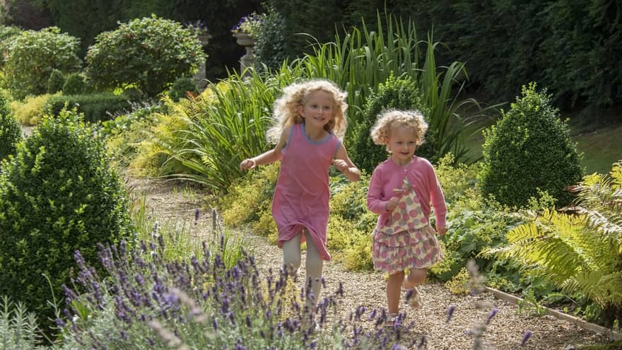 Two children in pink dresses running outside.