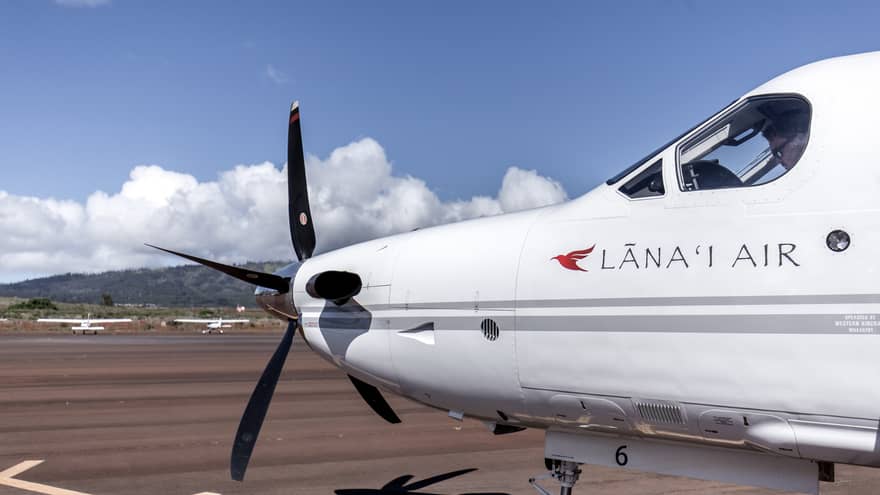 Passenger plane marked Lana'i Air (nose, front propeller and view of pilot in cockpit window), mountains in background