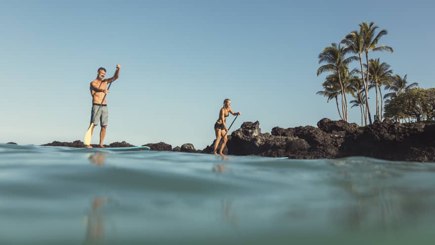 View from ocean looking up at two people on stand-up paddleboards near shore 