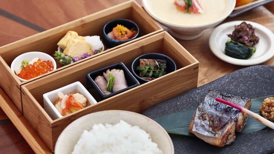 A close up of a Japanese Breakfast on a natural wooden tray – sushi, chopsticks, sashimi, caviar and peaches