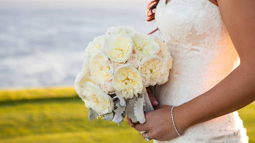 Bride holding wedding bouquet with white flowers near ocean