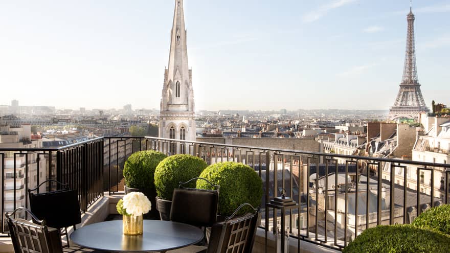 Patio dining table with white roses, potted shrubs iron balcony overlooking Paris rooftops, cathedrals
