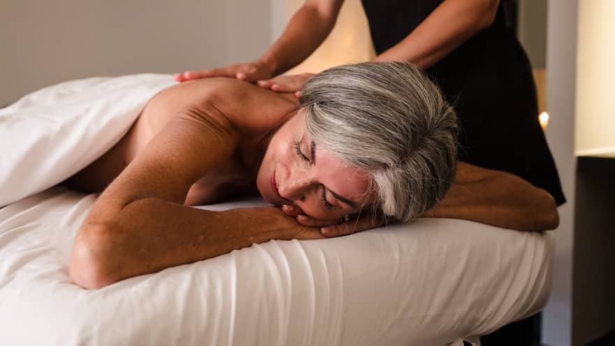 Person lies face down on massage table as therapist in black uniform performs massage