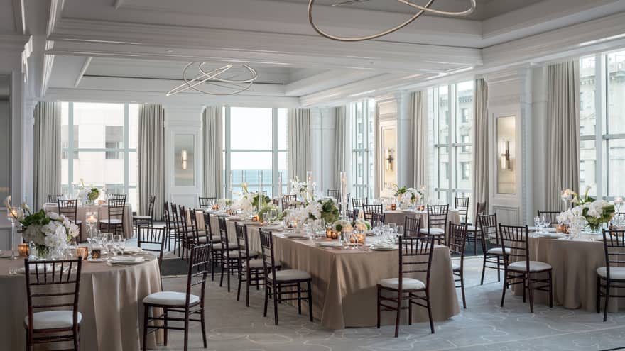 Ballroom with high ceilings and large windows, one long table surrounded by round tables