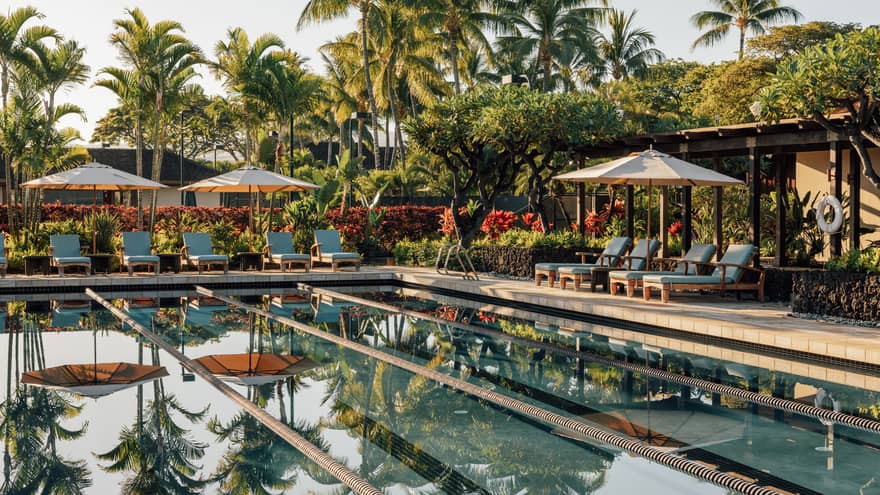 Outdoor lap pool with tropical palm trees and lounge chairs at Four Seasons Resort Hualalai, Hawaii