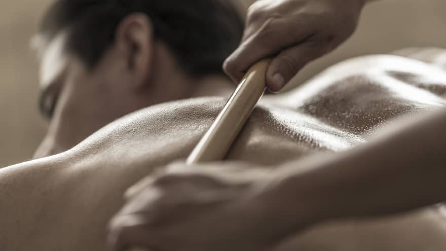 A spa attendant uses a tool to massage a guest's back